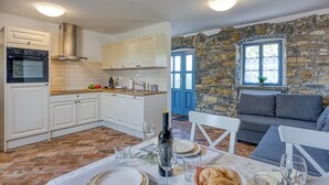 Une cuisine moderne avec des meubles blancs, un four encastré et un mur en pierre situé à côté d’un canapé gris.