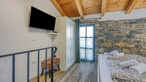 A bedroom with a stone wall, a bed with a patterned bedspread, a television mounted on the wall, and a wooden ceiling. - Istrian Casa Pr Marici Relaxing Vineyard, Koper, Slovenia (Koper)