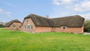 Une maison traditionnelle en briques, avec un toit de chaume, un petit porche et une balançoire.