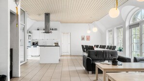 Une cuisine moderne avec des meubles blancs, un îlot central et un coin repas comprenant un canapé en cuir noir et une table en bois.