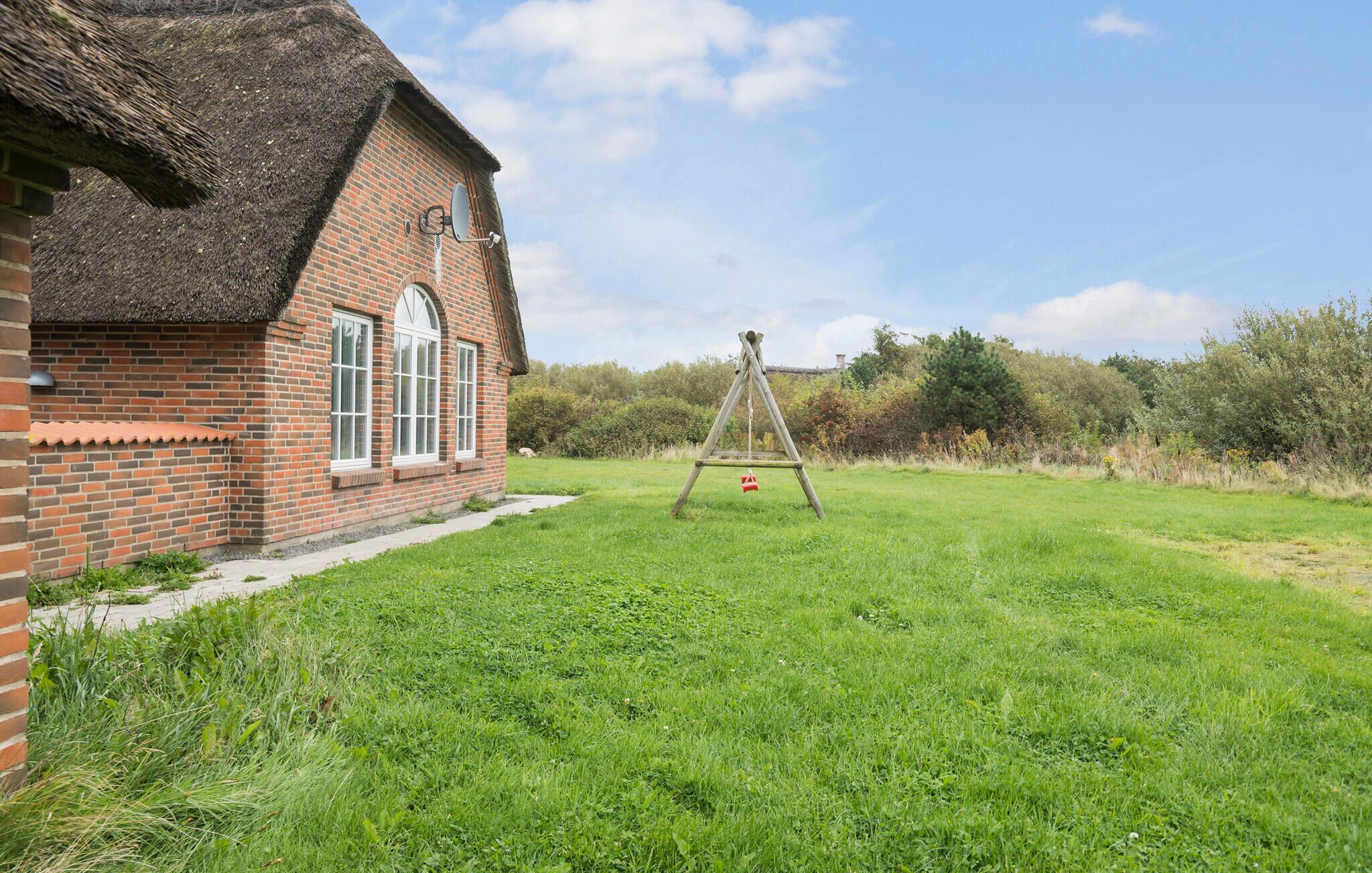 Une maison en briques avec un toit de chaume, une balançoire et une cour couverte d’herbe.