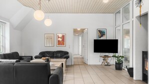 Un salon moderne avec un canapé en cuir noir, une table basse en bois et un téléviseur à écran plat fixé au mur. Une cheminée se trouve à droite et une plante en pot dans le coin.