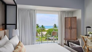 A hotel room with a large bed, a view of the ocean, a balcony with a chair, and a wooden wardrobe.