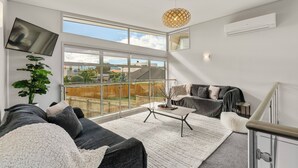 A modern living room with a large window, a flat-screen TV, a potted plant, a grey sofa, and a coffee table. - Lake Taupo Gem (Taupo)