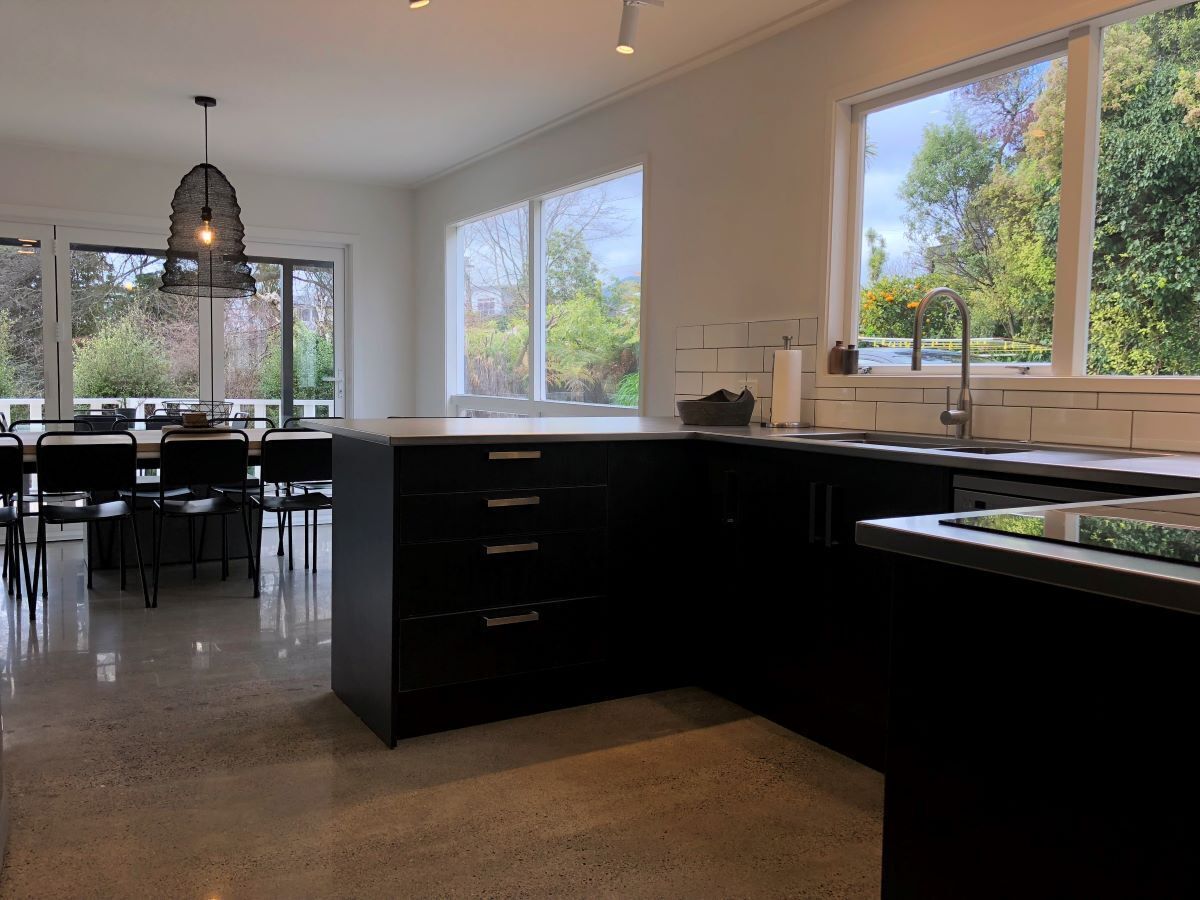 A modern kitchen with a central island, large windows, and a dining area with chairs.