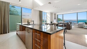 A modern kitchen with a large island, a dining area with a view, and a living space with a sofa and a coffee table.