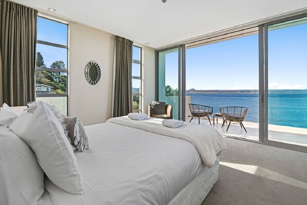 A bedroom with a large bed, two chairs, and a view of the sea.