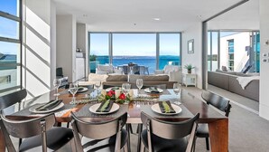 A modern dining room with a large table set for six, overlooking a scenic ocean view.