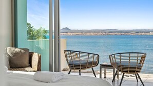A balcony with a bed, two wicker chairs, and a view of the sea.