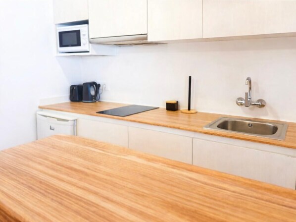 A kitchen with a wooden countertop, a microwave, a coffee maker, a sink, and a black electric kettle. - Enjoy Cala Porter - Apto en Complejo Vacacional (Cala'N Porter)