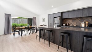 Una cocina moderna con encimera oscura, taburetes de bar y un área de comedor con mesa y sillas de madera.
