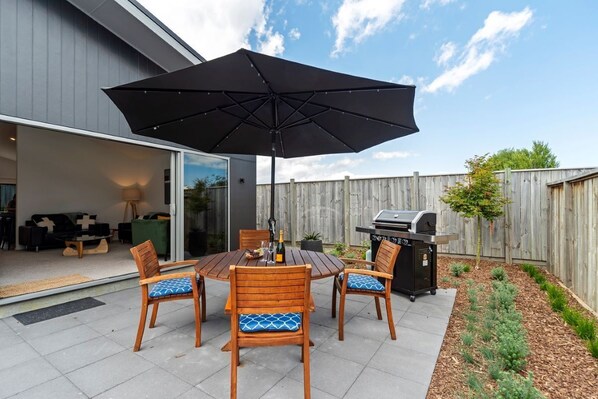 An outdoor patio with a round table, four wooden chairs, and a large black umbrella.