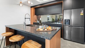 A modern kitchen with a central island, bar stools, a built-in oven, and a refrigerator. - CatchN'Relax with Hot Tub (Taupo)