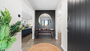 A modern hallway with a dark wooden door, a round mirror above a console table, and a large plant on the left. - CatchN'Relax with Hot Tub (Taupo)