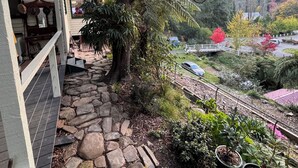 A stone pathway leading to a house with a large tree, surrounded by lush greenery and a view of a valley. - Cosy Mountain retreat in a historic old gold mining town (Walhalla)