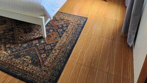 A hotel room with a bed, a nightstand with a lamp, a wooden floor, and a patterned rug. - The carmelence place by cerilos (Tagaytay)