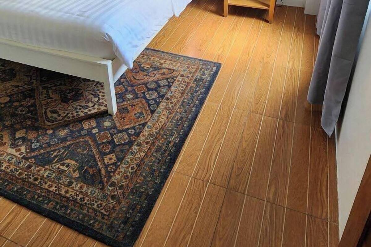 Une chambre d’hôtel avec un lit, une table de chevet avec une lampe, un plancher en bois et un tapis à motifs.