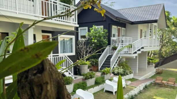 A two-story building with a balcony, a staircase, and a garden area with white chairs. - The carmelence place by cerilos (Tagaytay)