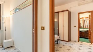 Une chambre d’hôtel avec un sol carrelé, un lit, une armoire et une salle de bain visible à travers une porte ouverte.