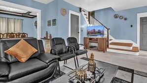 Sala de estar con un sofá de cuero negro, una mesa de centro con objetos decorativos, un televisor y una escalera que lleva a otro nivel.