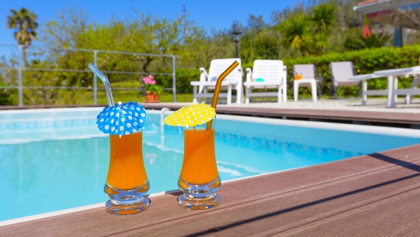 Two drinks with umbrellas on a poolside table.