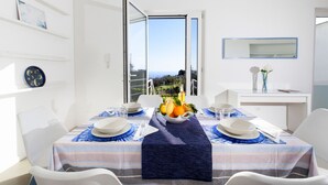 A dining area with a table set for two, a view of the outdoors, and a white interior with a blue-striped tablecloth.