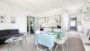 A modern living room with a grey sofa, a glass coffee table, and a dining area with a table set for four.