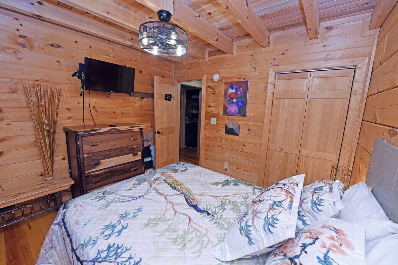 A wooden cabin bedroom with a bed, dresser, and a mounted TV.
