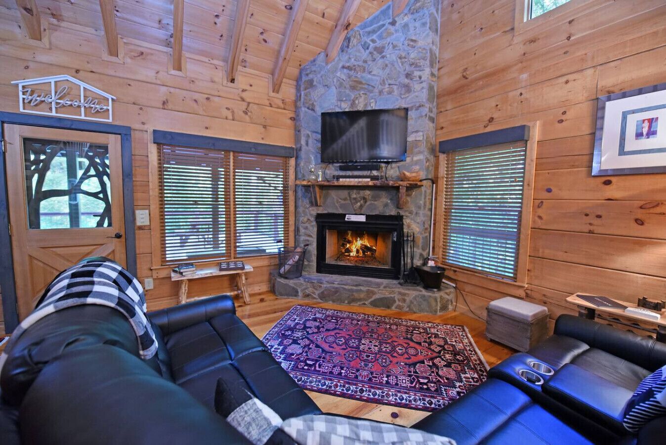 A cozy cabin interior with a stone fireplace, wooden walls, and a television mounted above it.