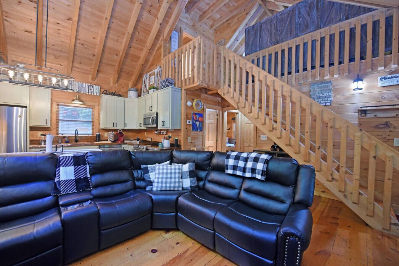 A cozy cabin interior with a wooden staircase, a sectional sofa, and a kitchen area.