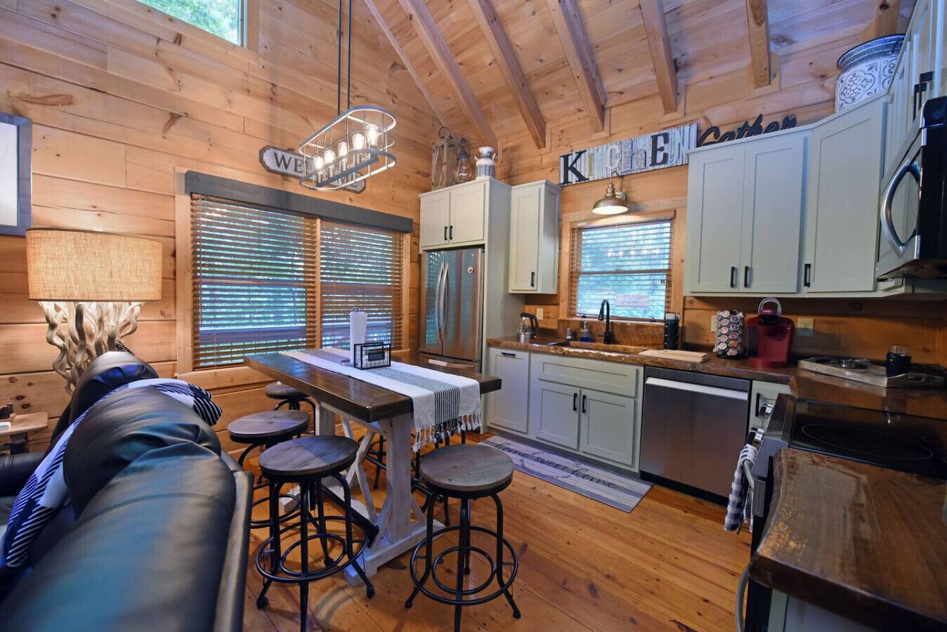 A cozy cabin-style kitchen with wooden walls, a bar area with stools, and a refrigerator.