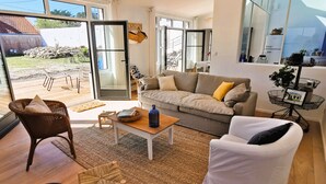 A spacious living room with a sofa, chairs, a coffee table, and a large sliding glass door leading to an outdoor area. - Dimitri’s workshop 500m from the beach (Barbâtre)