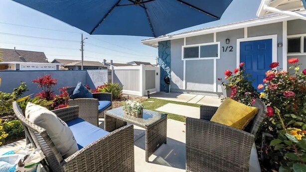 Een terras met rieten meubels, een grote parasol en een huis met een blauwe deur.