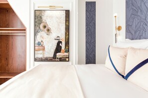 A hotel room with a large bed, a wooden wardrobe, a door with a decorative mirror, and a wall with a textured pattern.