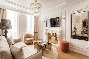 A spacious living room with a modern sofa, a round coffee table, a comfortable armchair, a fireplace, and a large TV mounted above it.