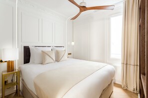 Una cama grande con ropa de cama blanca, un cabecero de madera y un ventilador de techo.