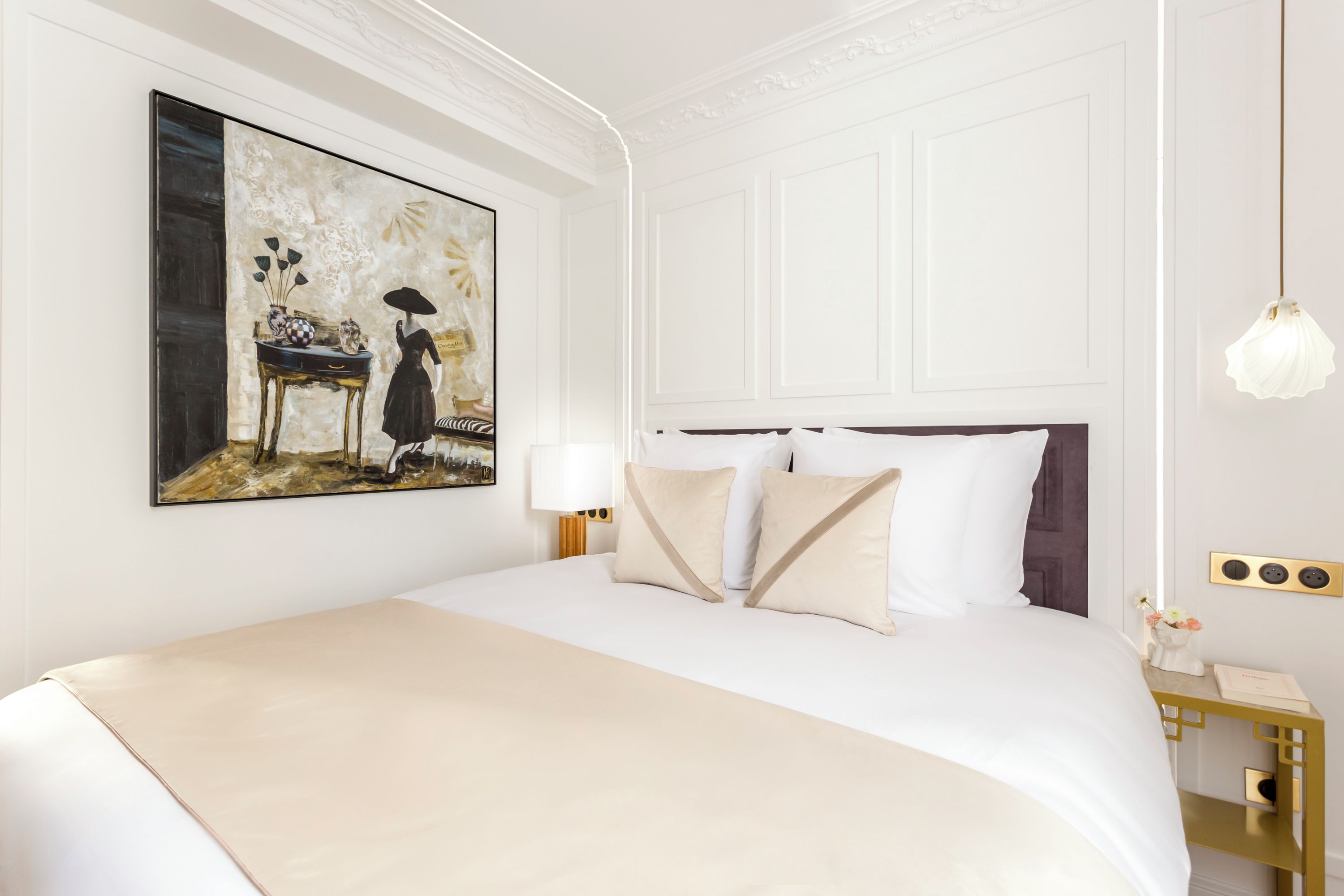 Quarto bem arrumado com uma cama grande, um quadro na parede, mesa de cabeceira com abajur e luminária decorativa.