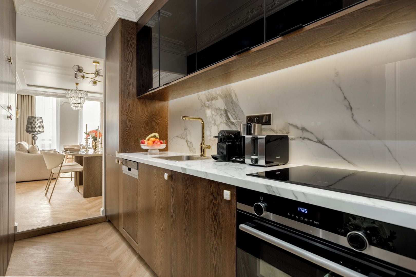 A modern kitchen with a marble countertop, built-in oven, and coffee maker.
