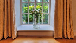 A window with a clear view of greenery outside, a vase with flowers on the windowsill, and curtains on either side. - Stunning 5-Bed Period Home,  Gardens & Tennis Court (Malahide)