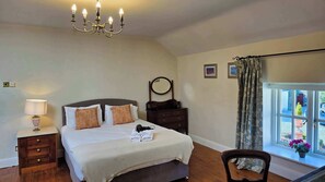 A bedroom with a bed, bedside table, lamp, dresser, mirror, and a window with curtains.