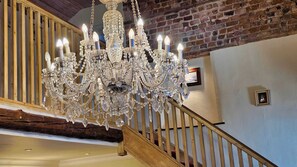 A grand chandelier with multiple lights hanging from the ceiling in a room with exposed brick walls and wooden beams.