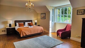 A bedroom with a bed, bedside lamps, a chandelier, a window with a view, a red chair, and a rug. - Stunning 5-Bed Period Home,  Gardens & Tennis Court (Malahide)