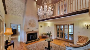 A spacious living room with a fireplace, a chandelier, and a high ceiling with exposed beams.