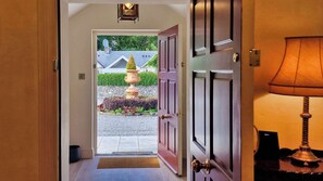 A hallway with a wooden door leading to a garden area with a fountain.