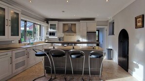 Une cuisine moderne avec des meubles blancs, un îlot central doté de tabourets et une grande fenêtre qui laisse entrer la lumière naturelle.