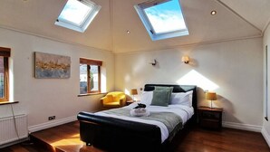 Une chambre à coucher avec un grand lit, des fenêtres de toit, un fauteuil jaune et un tableau accroché au mur.