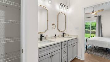 A modern bathroom with two sinks, a vanity with drawers, and a large mirror with lights.