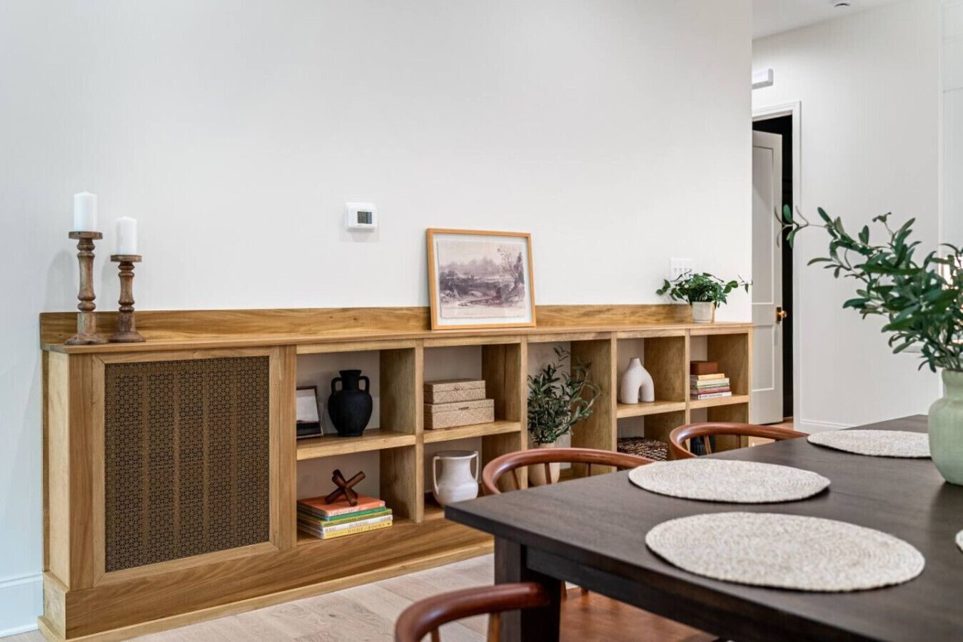 A dining area with a wooden console table, chairs, a framed picture, and a potted plant.