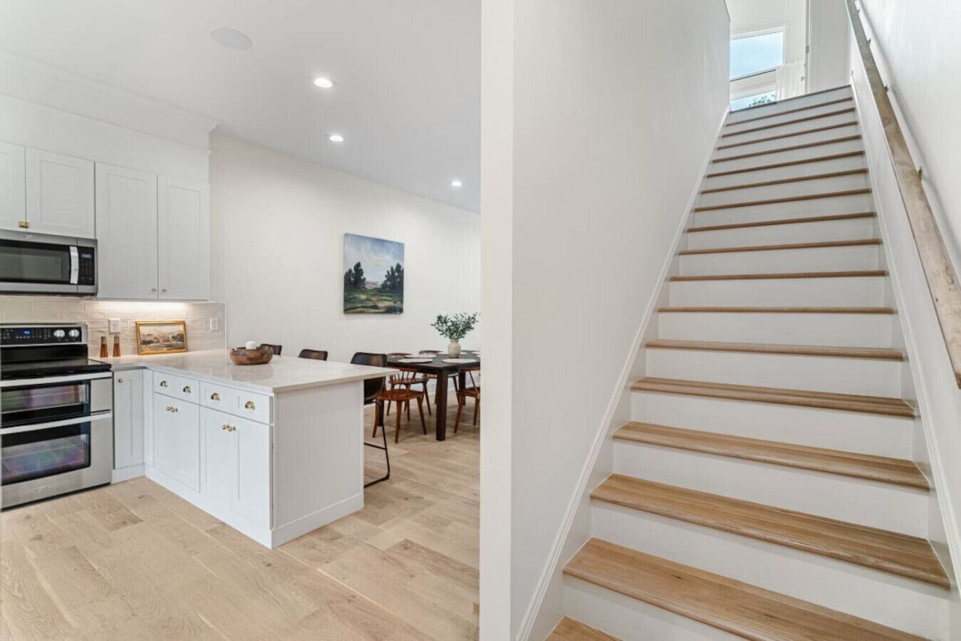A modern kitchen with white cabinetry, a central island, and a dining area with wooden chairs.