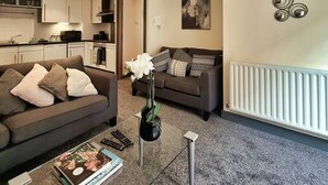 A living room with a sofa, a coffee table with a magazine, and a vase with flowers. - Lovely One Bed Apartment in Hip End of Temple Bar (Dublin 8)